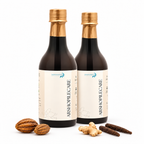 Two dark glass bottles of Sanadana Arshopilecare with gold caps and cream labels, displayed on a white background with ginger, turmeric, and sandalwood pieces.